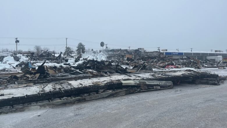 Debris and wreckage from a fire lays scattered across a snowy ground. 