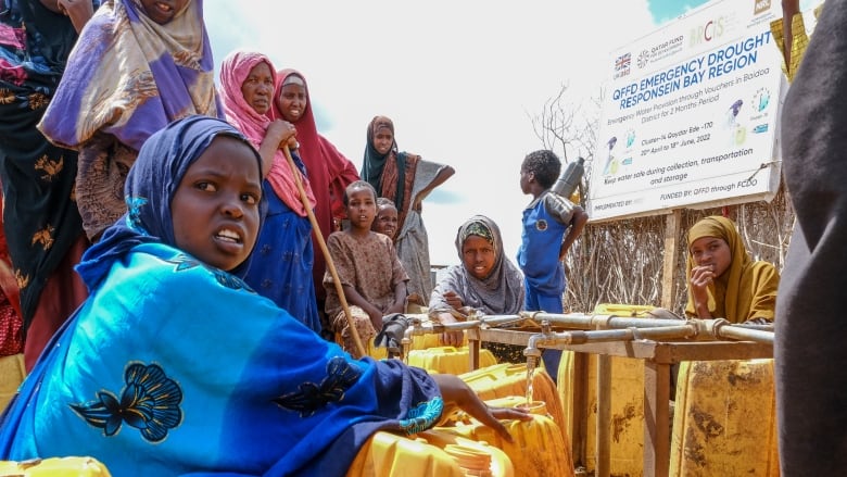 Several Somalis, one stooping down, collecting water in jerry cans. 