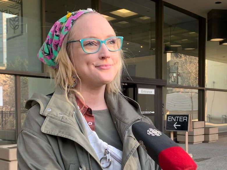 A woman wearing a bandana, turquoise eyeglasses and a green coat speaks outside the Edmonton courthouse.