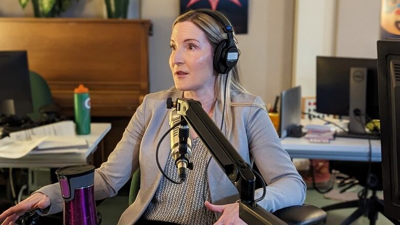 A woman sits at a microphone in a radio studio.