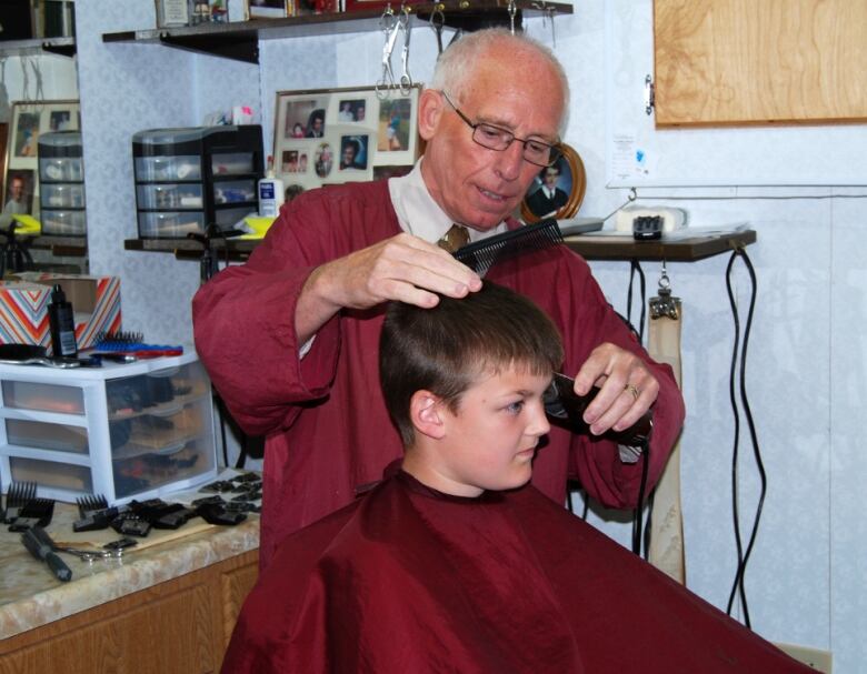 A man cuts the hair of a child sitting in a barber's chair.