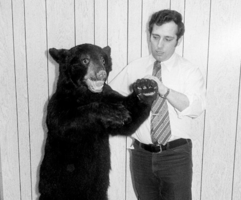 A man stands holding the paw of a taxidermized black bear. 