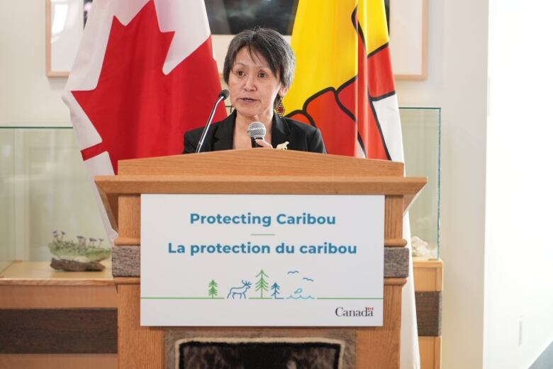 A woman speaks into a microphone at a lectern.