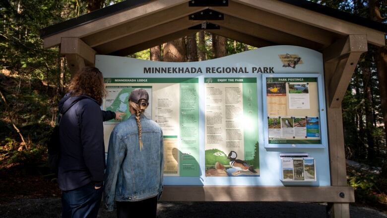 Two people point at a park information board with the words 'Minnekhada Regional Park' visible.