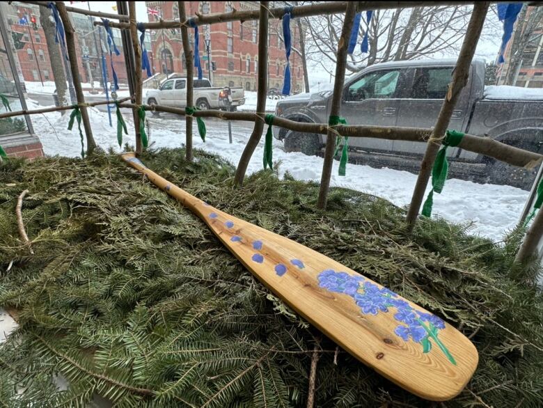 A wooden paddle with painted blue flowers on it rests on a pile of pine branches.