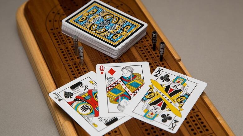 Indigenous-themed playing cards in the form of a King, Queen and Joker sit on a cribbage board.