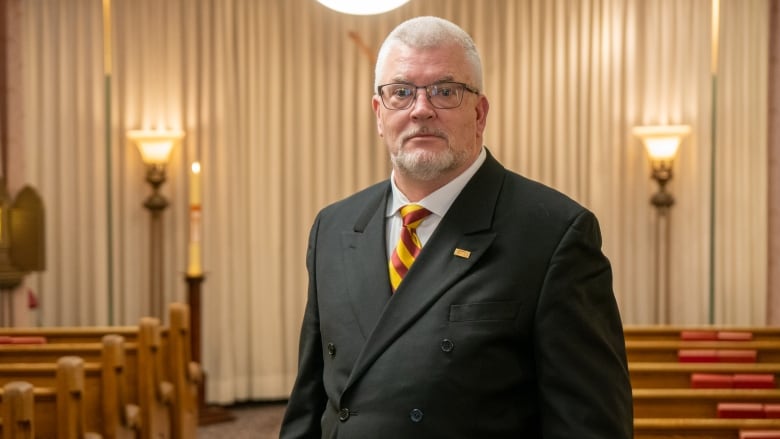 A man in a suit stands in a funeral chapel.