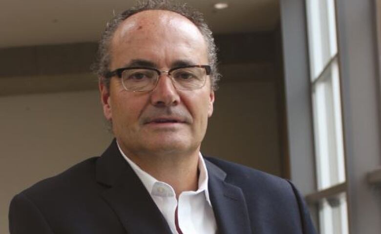 A balding man in a white shirt and blue sports jacket poses for a photo.