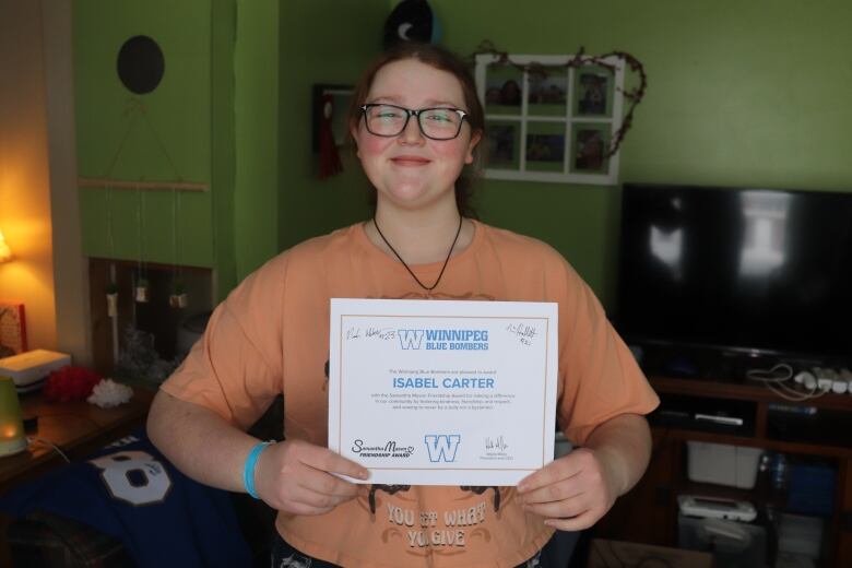 A woman stands with a award certificate that reads her name 'Isabel Carter'