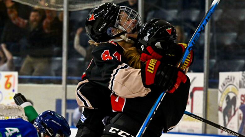 Two female hockey players hug on the ice while celebrating a goal.