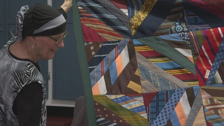 A woman holds up a quilt made of ties.