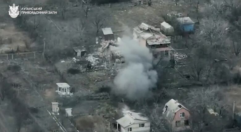 An aerial shot shows smoke rising from the ground and destruction to some buildings in what appears to be a residential area.