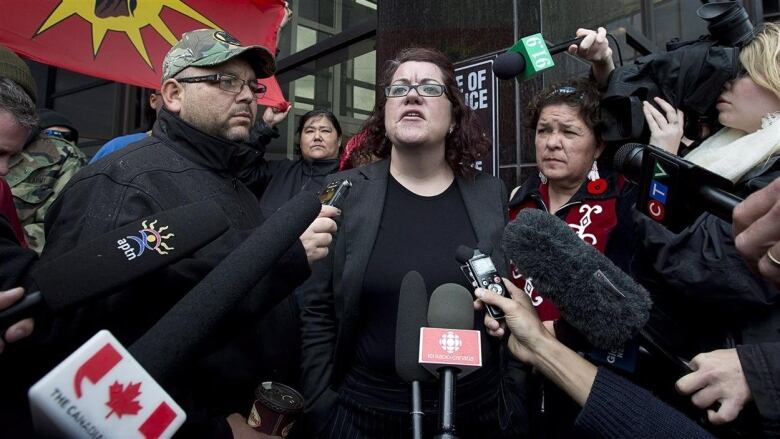 A femal lawyer speaking to media, surrounded by crowd