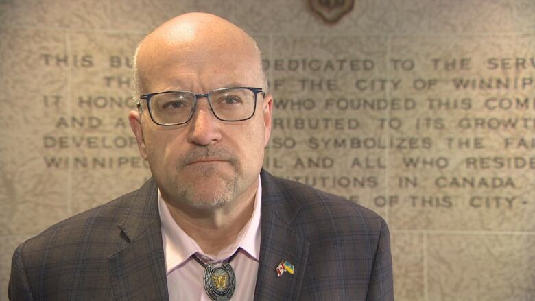 A head-and-shoulders image of a man with glasses in a suit and a dress shirt with a bolo tie.