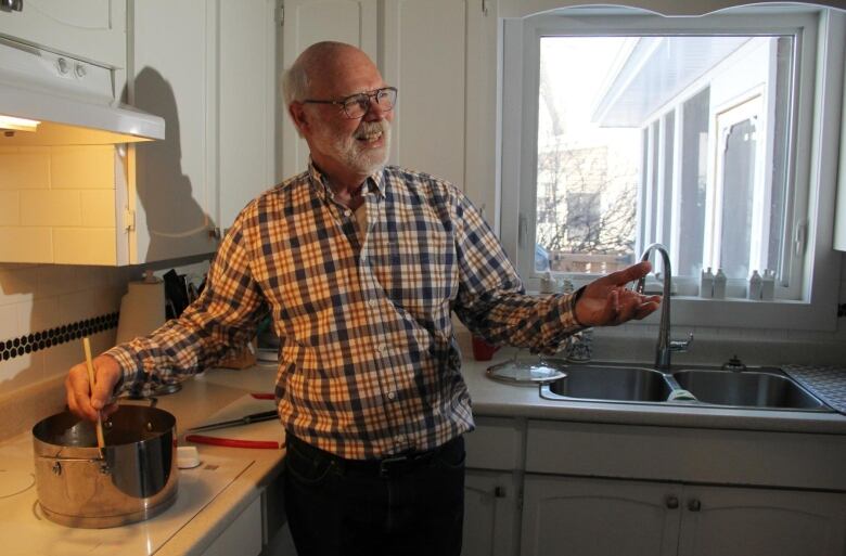 Gary Martens stirs food he's cooking in his pot with his right hand, while gesturing to another person in the room with his left hand.