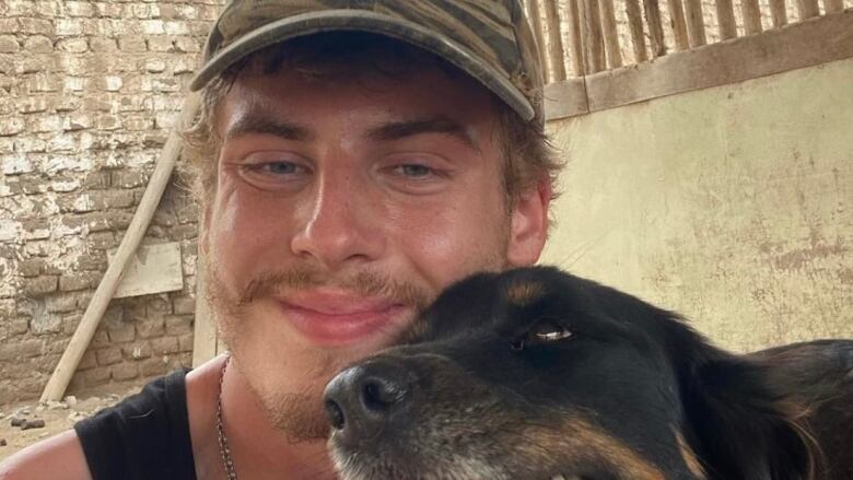 A young man in a baseball cap hugs a dog and smiles at the camera.