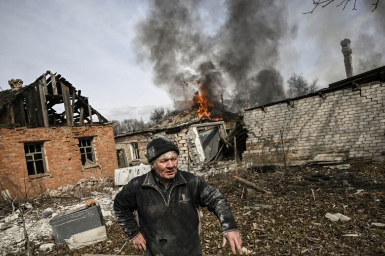 A man stands outside a burning house after it was hit by shelling in the Ukrainian town of Chasiv Yar.