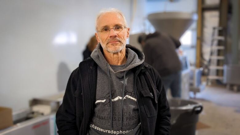 A man stands in a large building with a machine behind him making bait sausages 