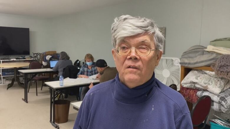 A man in a blue turtle neck with white hair and glasses. 