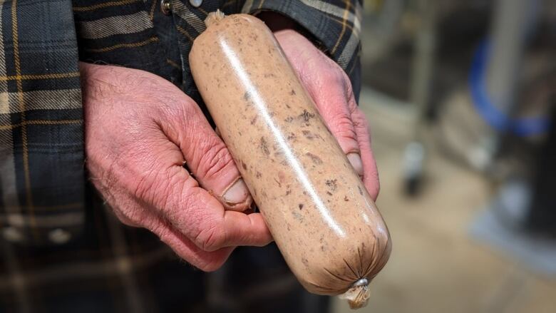 Hands hold a super-sized sausage filled with ground up fish and seal 