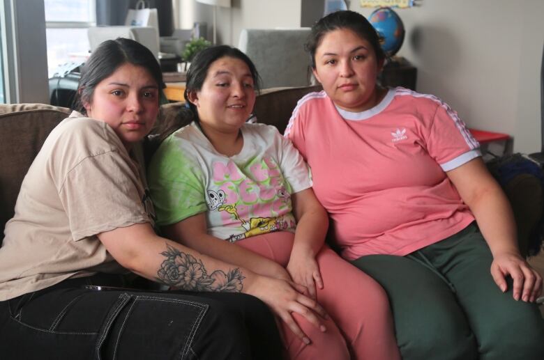 Three young women sit together on a couch. 