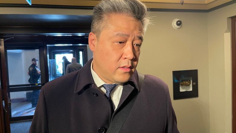 A man in a jacket, shirt and tie stands in a hallway.