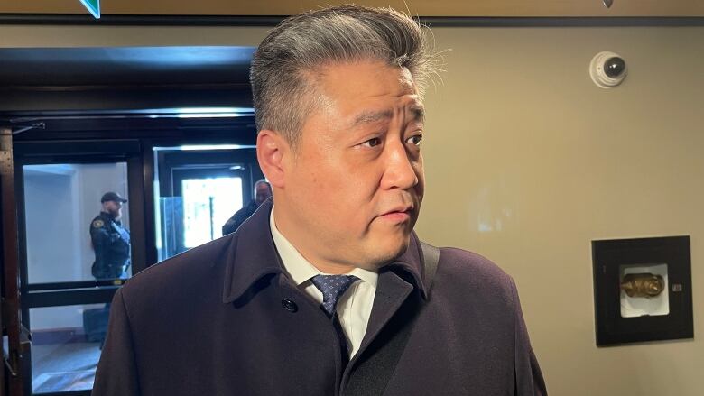 A man in a jacket, shirt and tie stands in a hallway.