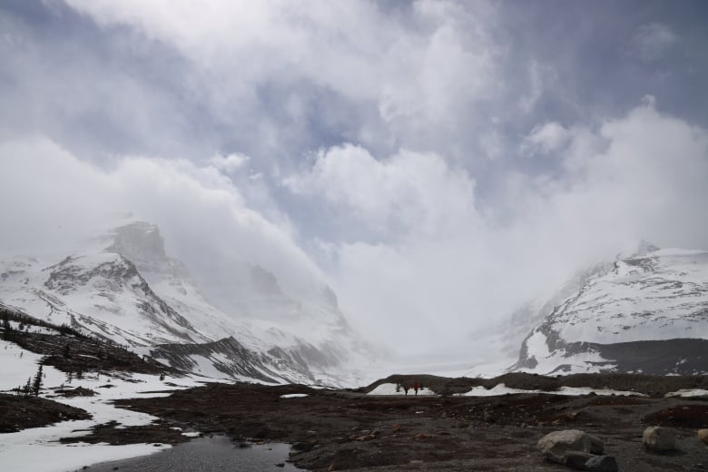 Blue sky and clouds hover above snow covered mountain peaks. 