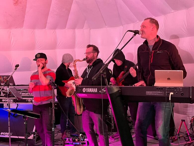 A band plays music live on stage under a white tent.