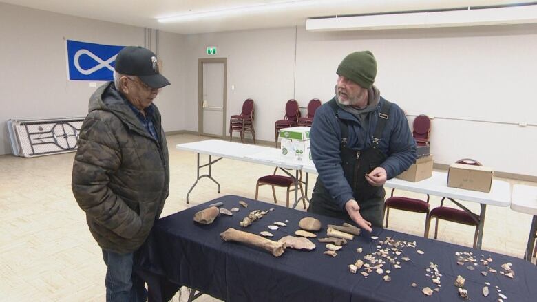 A man shows another man lithic and bone material displayed on a table.