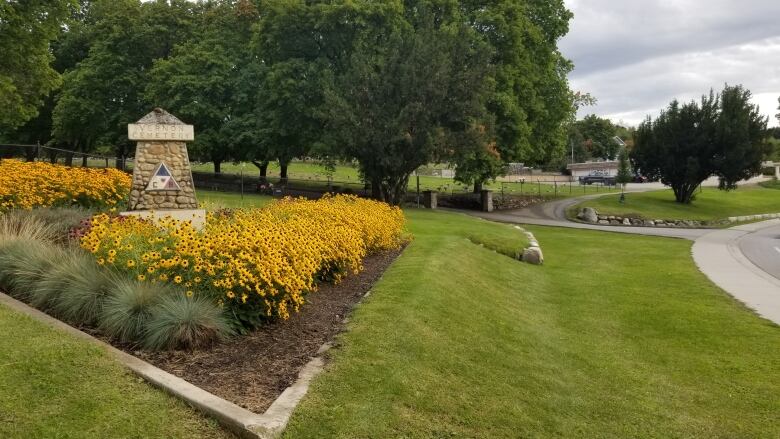 A photo of the lush green grass and landscaped entrance to the Pleasant Valley Cementary in Vernon, B.C. with trees and a entranceway in the distance. 