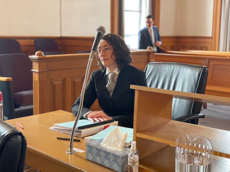 A woman with curly hair wearing black robes and a white shirt. She's sitting at a table in a courtroom.