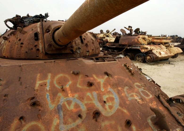 A rusted tank peppered with whole and the letters D and U spray painted on it.