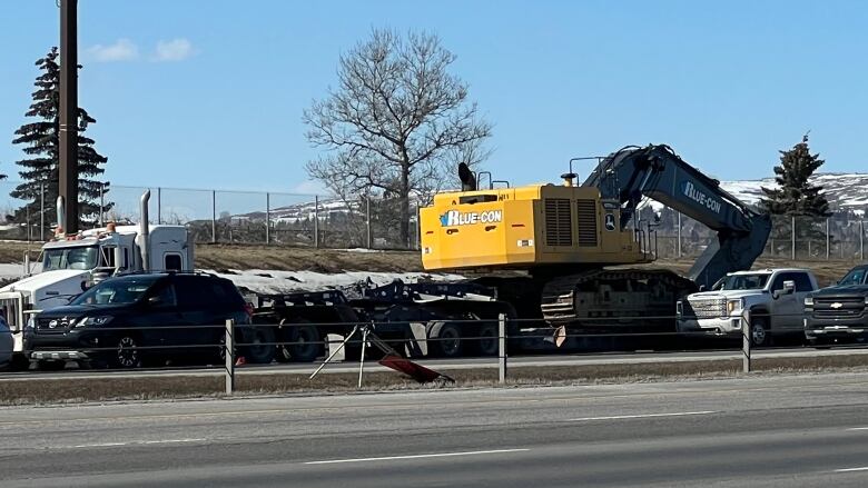 A yellow and black backhoe sits on Deerfoot Trail, surrounded by emergency vehicles. 