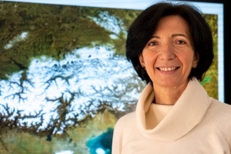 A woman stands smiling in front of a map featuring mountains. 