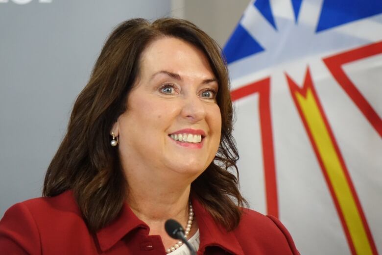 A smiling woman in a red blazer stands in front of the Newfoundland and Labrador flag.