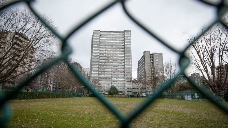 A highrise building is seen through a chainlink fence.