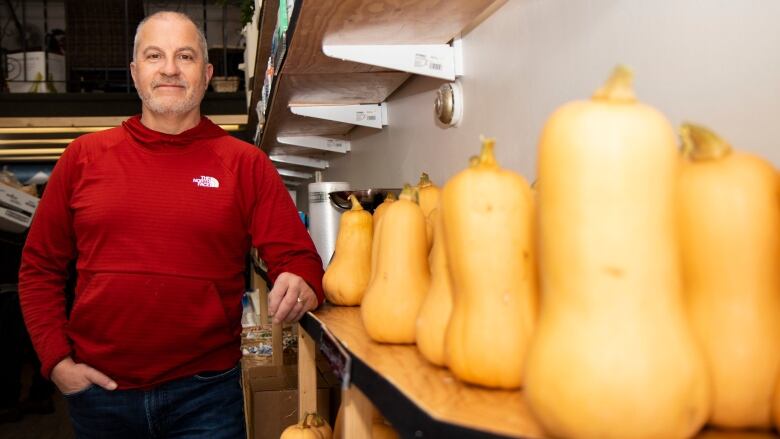 A man wearing a red shirt stands in a grocery store by some butternut squash.