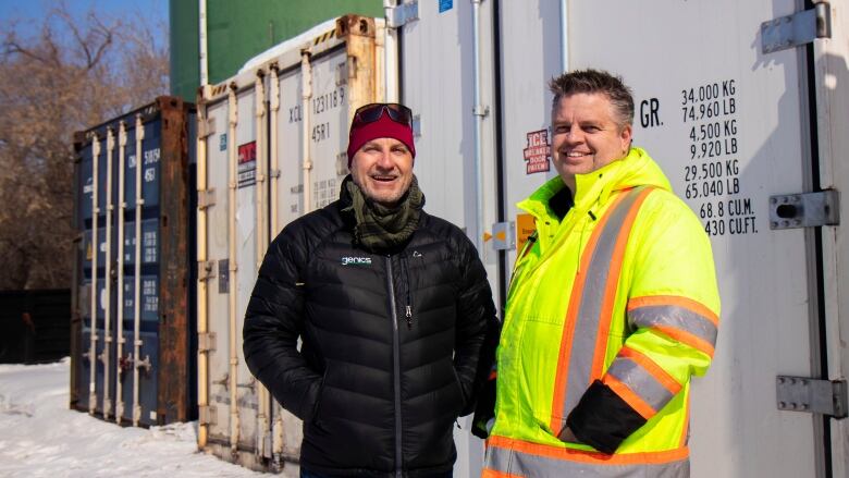 Two men stand outside in front of freight cars.