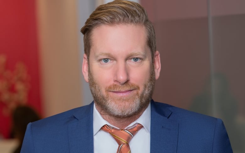 A headshot of a man facing the camera wearing a suit. 