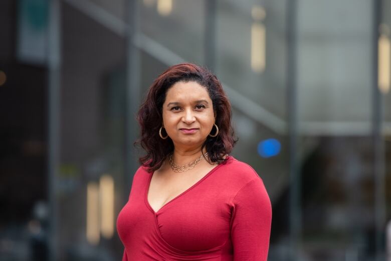 Williams looks at the camera in a red long sleeved shirt in front of a glass building. 