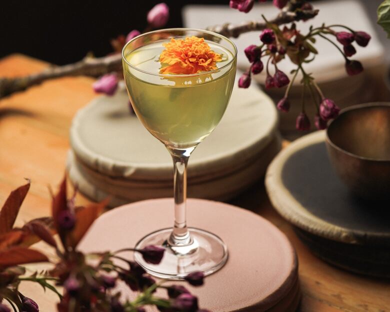 A green mocktail with an orange blossom garnish sits on a coaster.