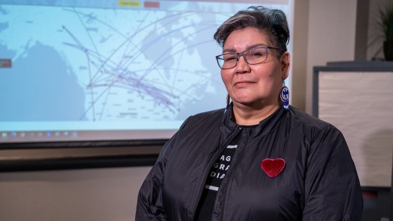 Colleen Hele-Cardinal poses beside the map showing how far Sixties Scoop survivors were taken.