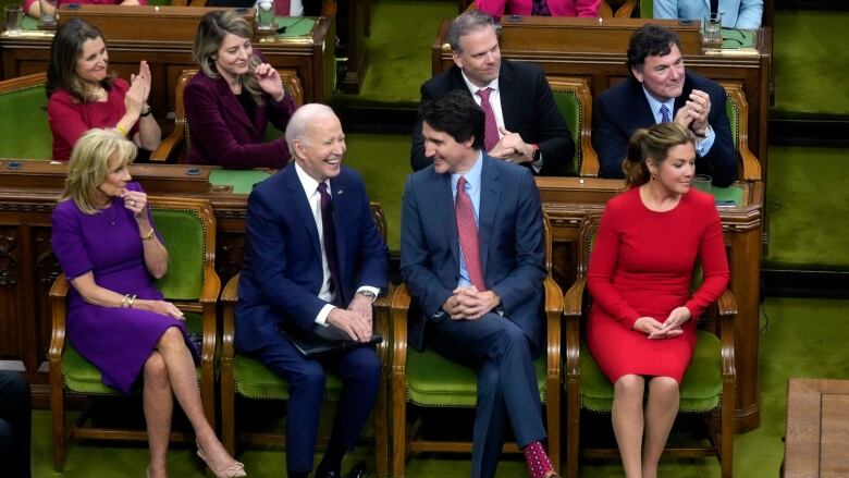 Eight people applaud and speak as they sit in chairs in the House of Commons.