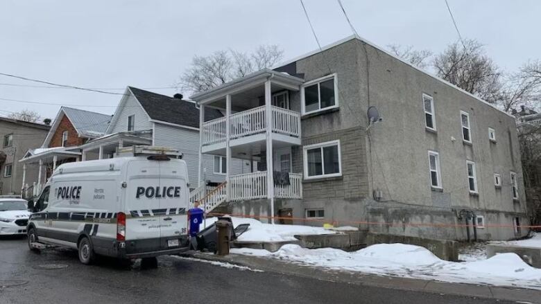 A police van is parked outside a grey apartment building.