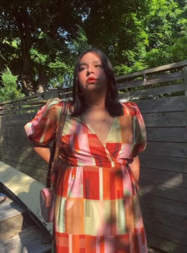 A young woman in a colourful dress stands in a park.