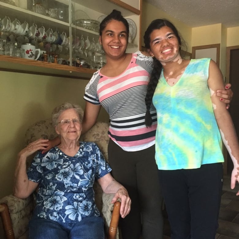 Two East Indian sisters link arms with each other and a seated white-haired woman. 