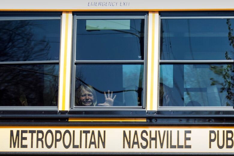 A child in a school bus weeps while placing their hand on the window.