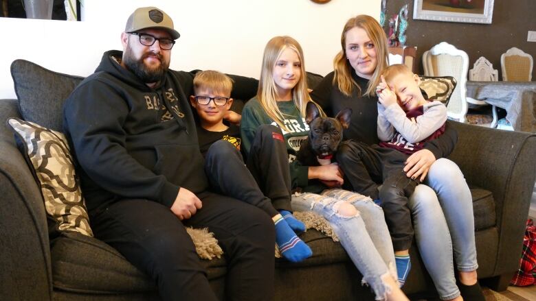 A family of five sits together on a couch.W