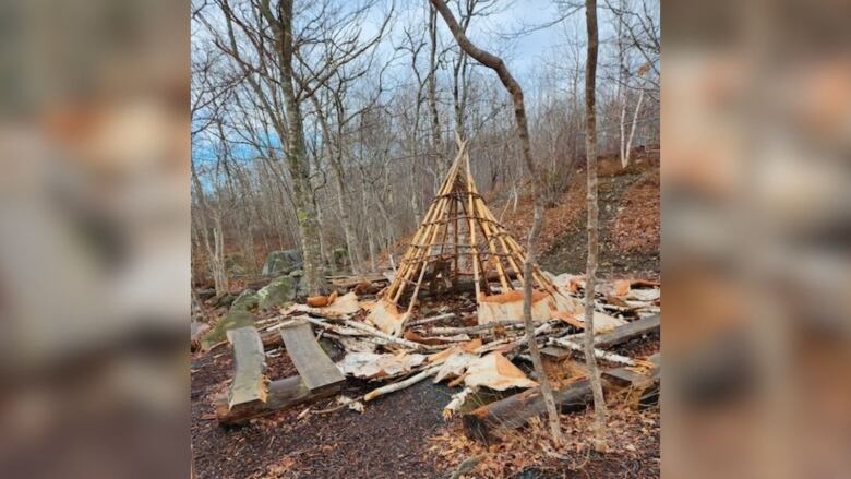 A triangular structure made of wood with bark on the ground around it.